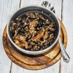 A small bowl filled with marinated mushrooms sitting on a round wooden board.