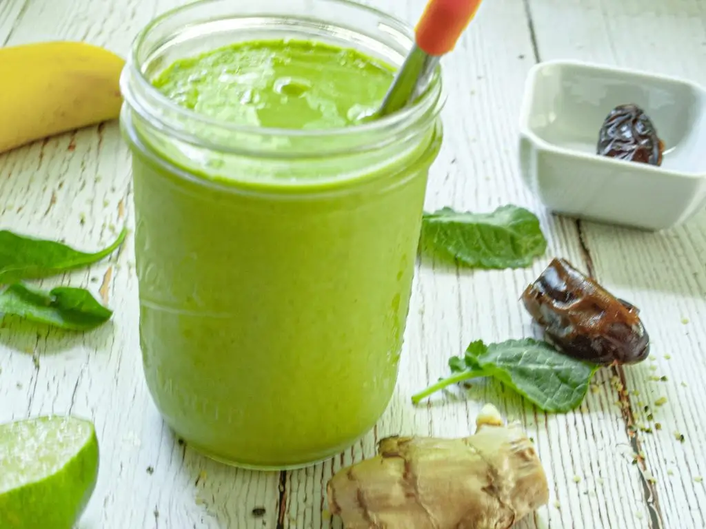 A green smoothie in a clear mason jar sits on a white wooden table.