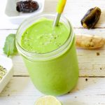 A vibrant green smoothie in a glass cup with metal straw.