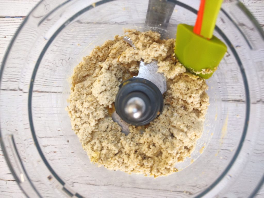 A green and red spatula scraping down the bowl of partially processed tofu ricotta.