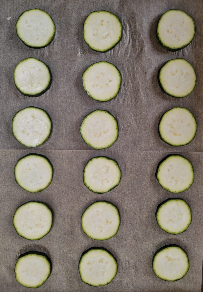 Three rows of sliced zucchini on a baking tray.