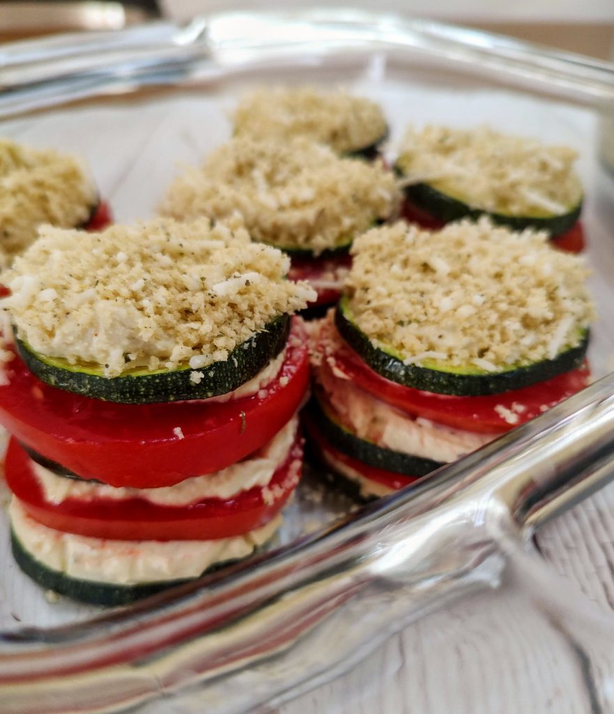 A glass baking dish full of unbaked zucchini stacks with a bread crumb topping.