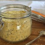 An open glass jar of vegan parmesan on a wooden table.